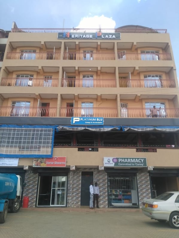Un immeuble à plusieurs étages doté de balcons, d’une pharmacie et d’un commerce appelé « Platinum Blu » situé au rez-de-chaussée.