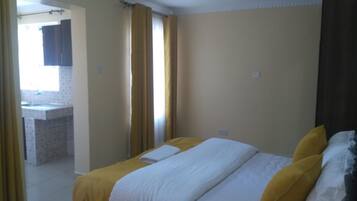 Une chambre à coucher avec un lit, une fenêtre avec des rideaux et une vue sur une salle de bain.