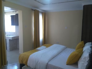 Une chambre à coucher avec un lit, une fenêtre avec des rideaux et une vue sur une salle de bain.