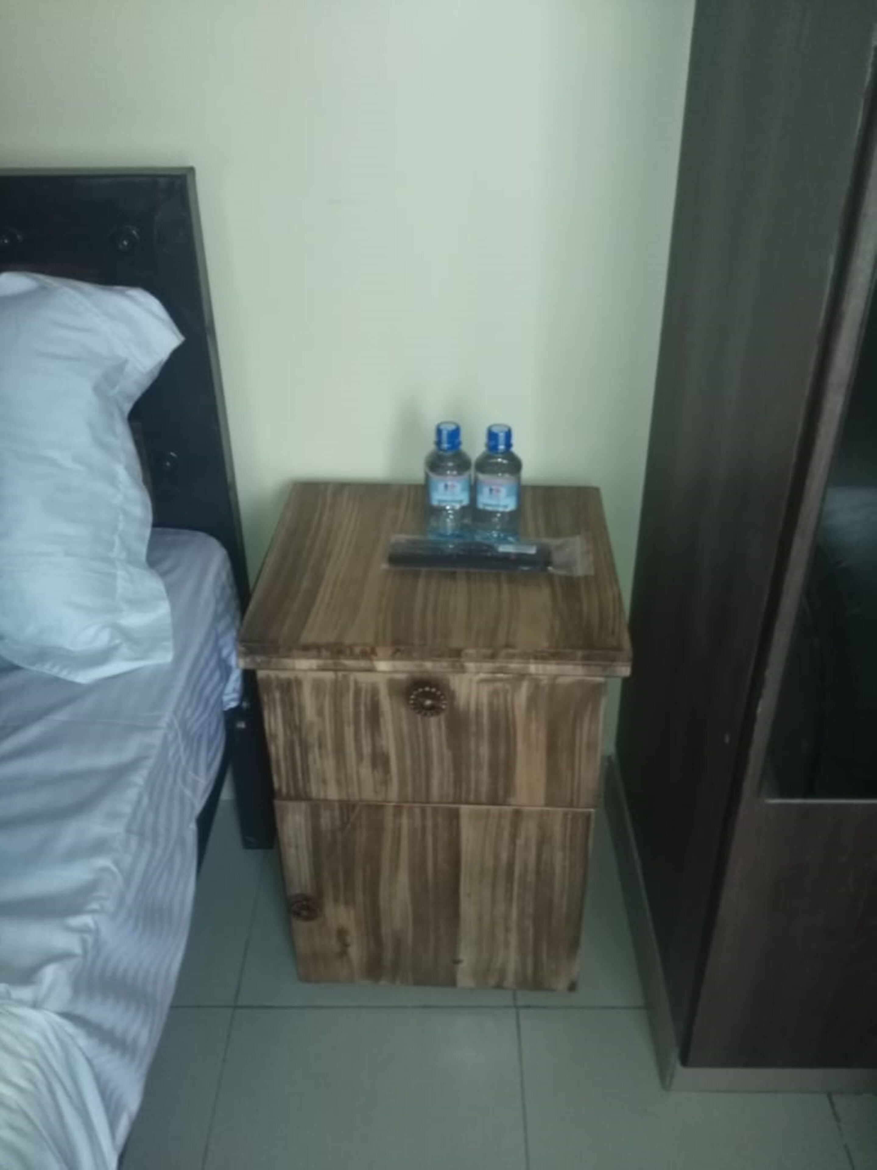 A small wooden nightstand with two bottles of water and a remote control.