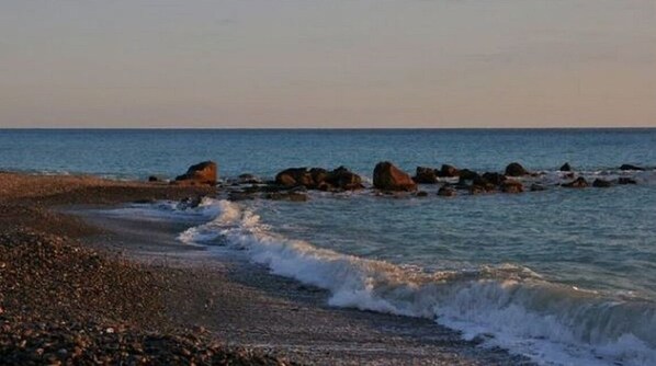 Experience the serene tranquility of a pebbly beach, surrounded by large rocks and a calm sea.