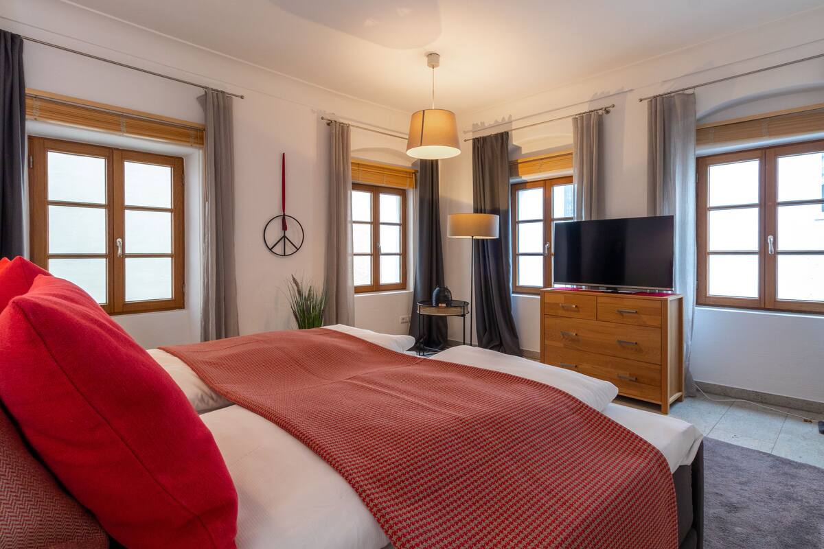 A hotel room with a large bed, a TV, a dresser, and a window with curtains.