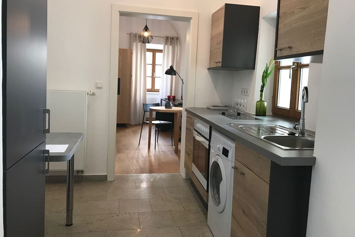 A compact kitchen with a washing machine, a dining area with a table and chairs, and a view into a living space.