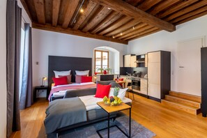 A modern bedroom with a large bed, a small table with fruit, and a kitchenette in the background. - BARONHAUS Aparthotel & Suites (Passau)