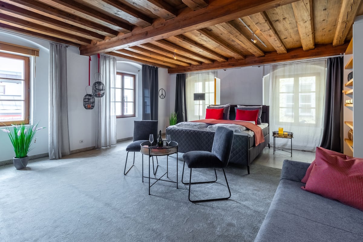 A modern bedroom with a bed, a sofa, a small table, and a potted plant.