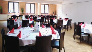 A dining area with multiple round tables set for meals, each with white tablecloths, red napkins, and black chairs. - Alcatraz am Japanischen Garten (Kaiserslautern)