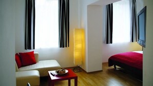 A hotel room with a sofa, a small table with a bowl of fruit, a bed with a red blanket, and a standing lamp. - Alcatraz am Japanischen Garten (Kaiserslautern)