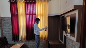 Un hombre ajustando un televisor en una habitación con un sofá, una mesita y cortinas.