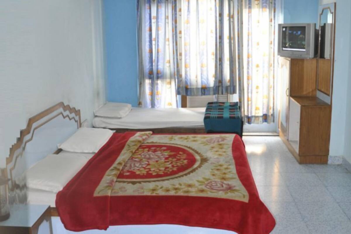 A bedroom with a bed, a wooden wardrobe, a small table, and a window with curtains.