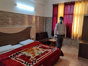 A hotel room with a bed, a sofa, a small table, and a nightstand. - Hotel Aashirwad (Reasi)