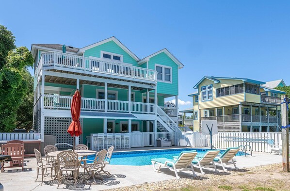 A two-story building with a pool, outdoor seating, and a staircase leading to the upper floor. - Family Tradition - Duck Landing, Oceanside, 130 Yds to Beach, Pool, Hot Tub, Tiki Bar (Duck)