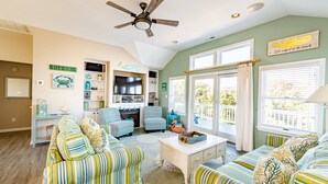 A living room with striped sofas, a ceiling fan, a television, and a view of the outdoors. - Family Tradition - Duck Landing, Oceanside, 130 Yds to Beach, Pool, Hot Tub, Tiki Bar (Duck)