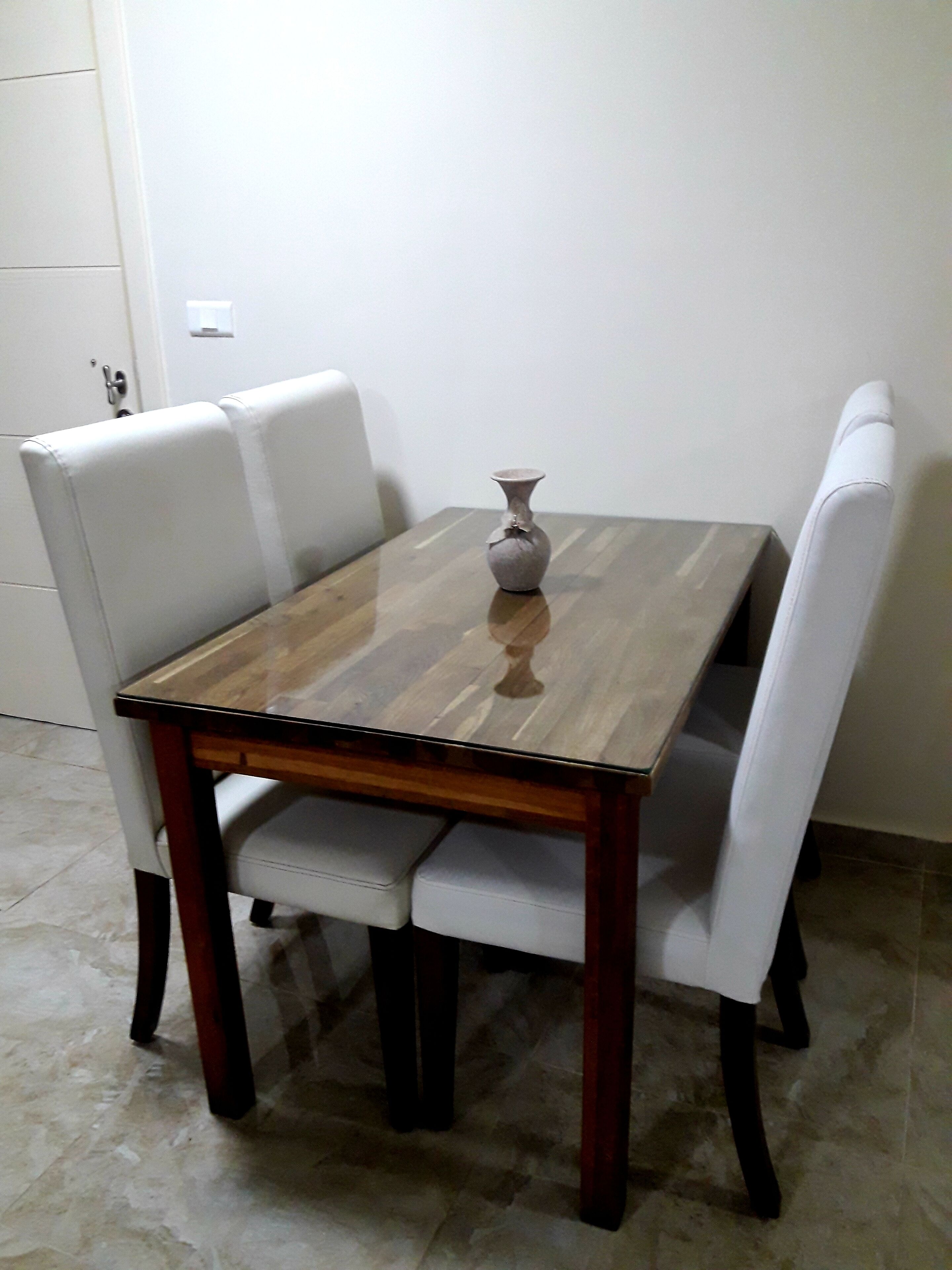Una mesa de comedor con un florero, rodeada de sillas blancas tapizadas.