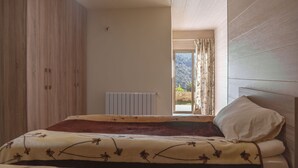 Un dormitorio con cama, un radiador, una ventana con cortinas y vistas al exterior.