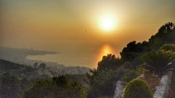 A coastal cityscape with a sunset over the water, featuring a mix of natural and urban landscapes.