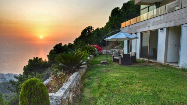 Una casa moderna con un patio que da a un cuerpo de agua durante el atardecer.