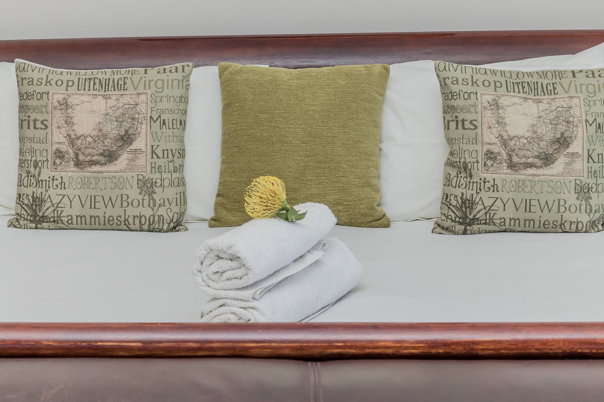 A neatly made bed with a rolled white towel and a green pillow with a yellow decorative element.