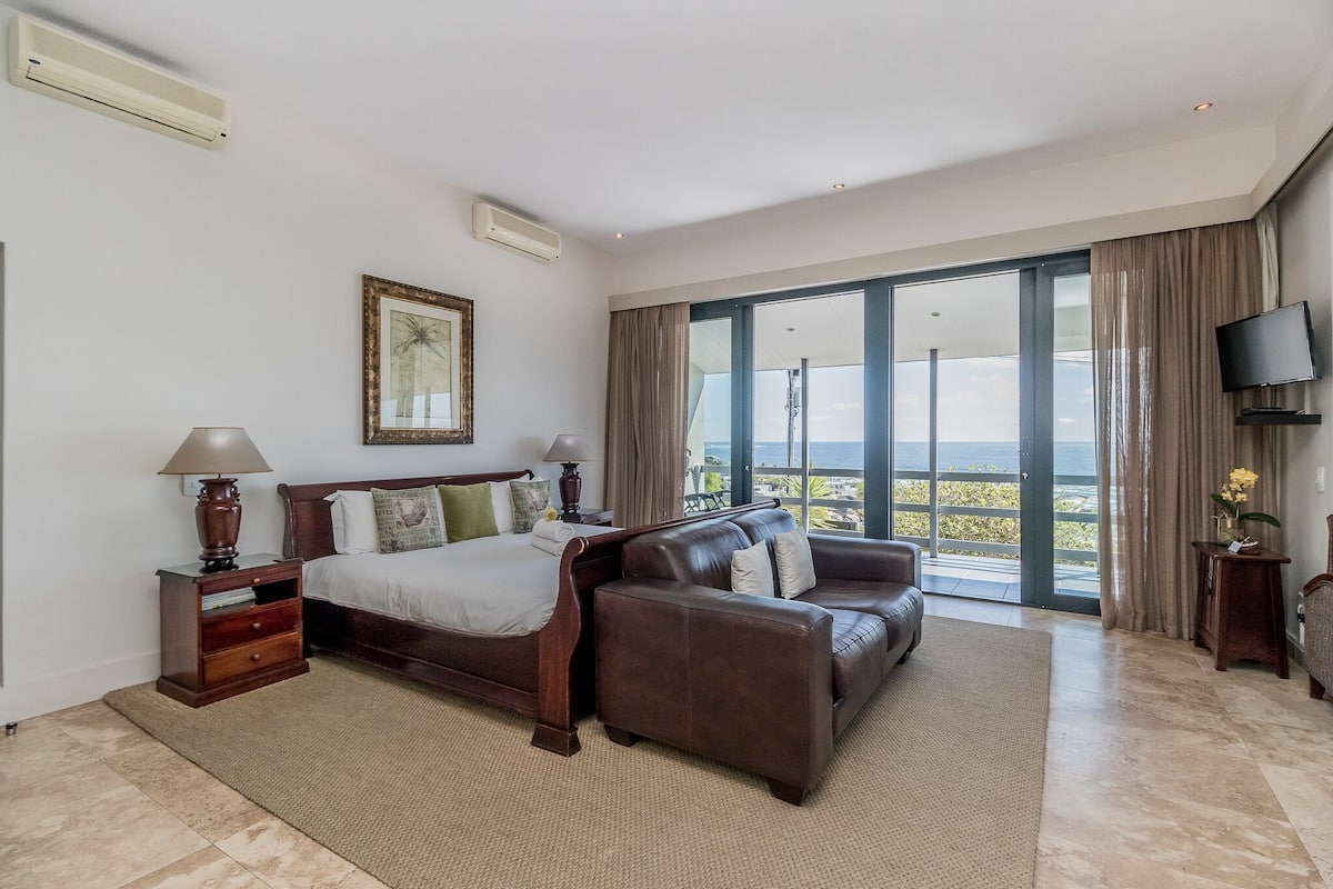 Quarto de hotel com cama, sofá, televisão e uma janela grande com vista.
