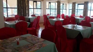 A conference room with multiple tables and chairs, large windows, and curtains. - Mash Park Hotel Kisii (Kadongo)