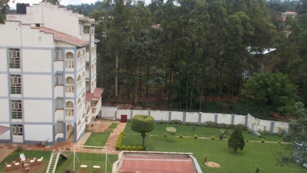 A multi-story building with a courtyard featuring a neatly trimmed lawn, a small tree, and a tennis court. - Mash Park Hotel Kisii (Kadongo)