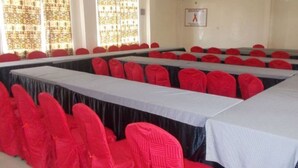 A conference room with rows of tables and red chairs. - Mash Park Hotel Kisii (Kadongo)