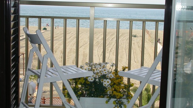 A balcony with two white chairs and a flower arrangement, overlooking a sandy beach with people in the distance. - Le Nereidi B&B (Margherita di Savoia)