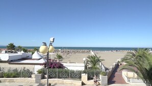 A beach view with a clear sky, a sandy beach, and a few people. There are buildings with balconies and a white fence in the foreground. - Le Nereidi B&B (Margherita di Savoia)