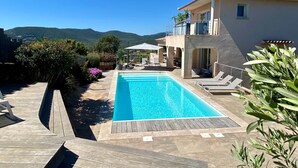 Uma piscina com deck de madeira, espreguiçadeiras e vista para montanhas.