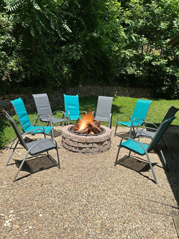 A circular stone fire pit with a fire burning, surrounded by four chairs with teal cushions. - Pinners Cove: Hot Tub, Fire Pit, Prime Location (Asheville)