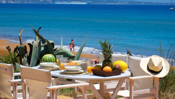 Ein Tisch ist reichhaltig mit Frühstücksleckereien gedeckt, mit Blick auf Strand und Meer.