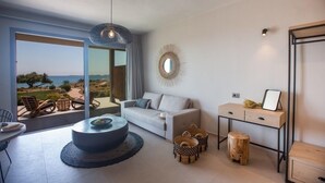 Ein modernes Wohnzimmer mit einer Couch, einem runden Tisch und Korbwannen. Ein großes Fenster bietet Blick auf das Meer.