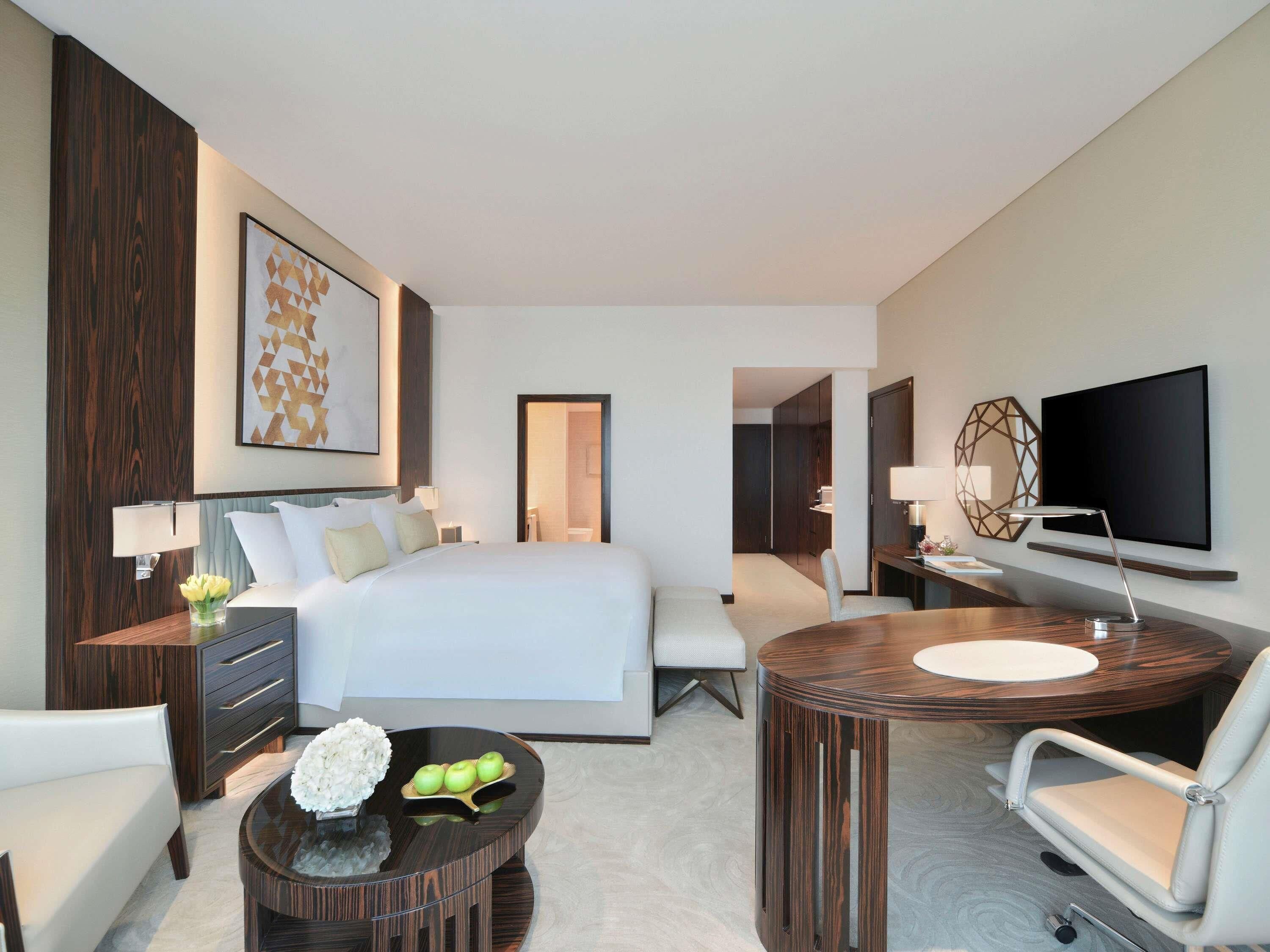 Une chambre d’hôtel moderne dotée d’un grand lit, d’un bureau avec une chaise, d’une télévision et d’une table basse ronde agrémentée d’objets décoratifs.