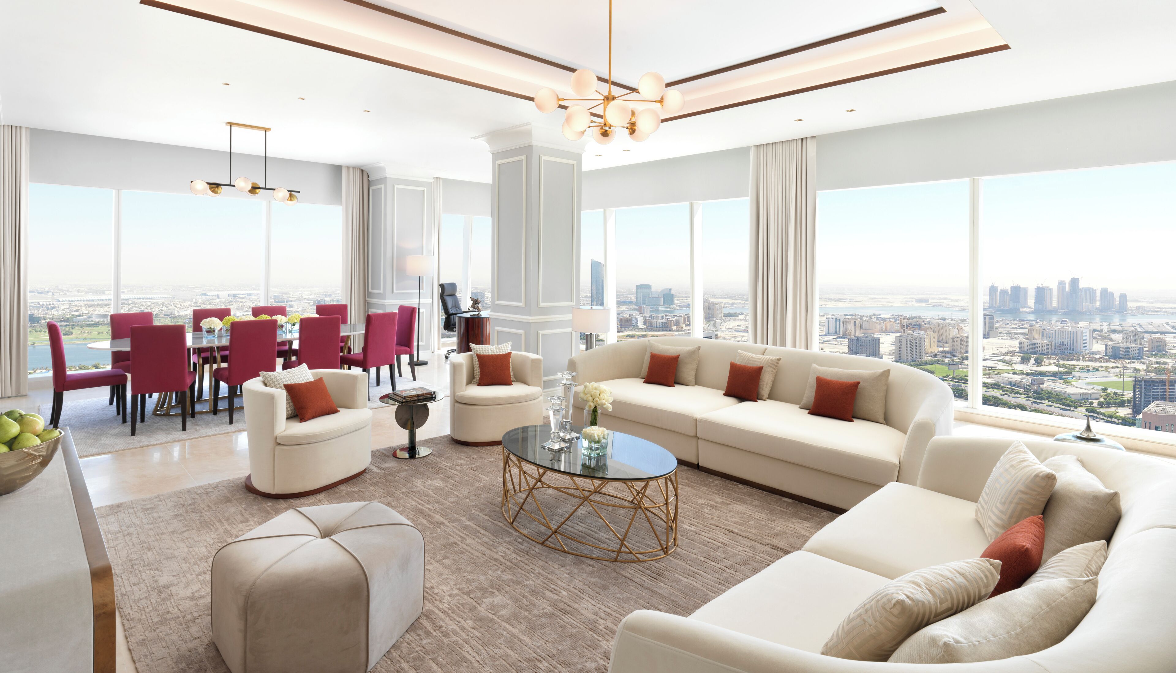 A spacious living room with a large sofa, a coffee table, and a dining area with red chairs and a white table.