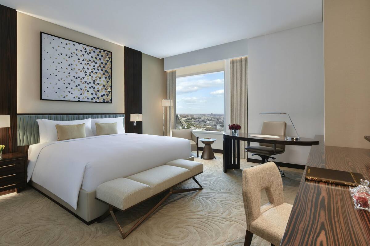 Una habitación de hotel moderna con una cama grande, un escritorio, una silla y vistas de la ciudad.