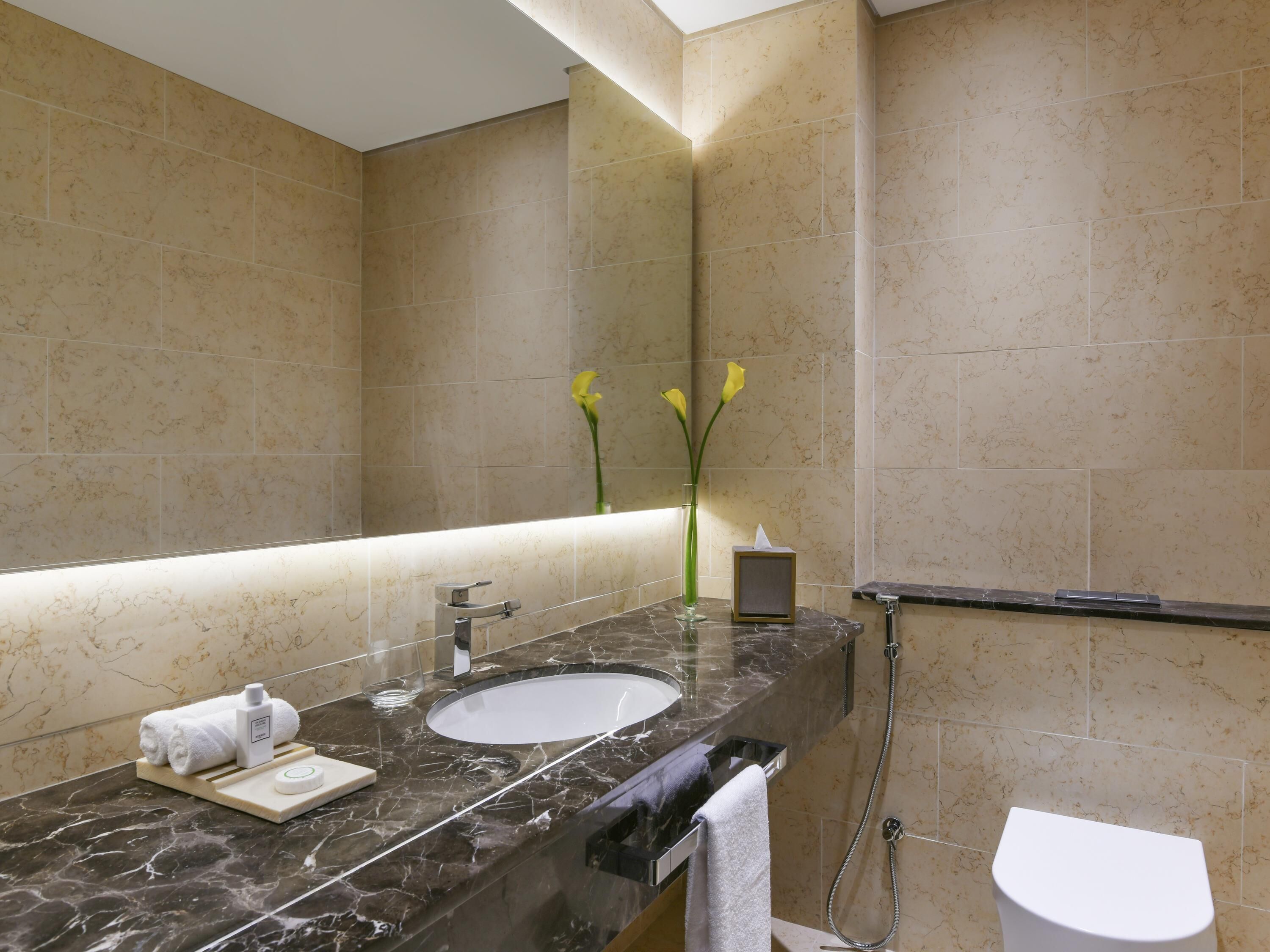 A bathroom with a marble sink, a towel rack, a glass of water, and a vase with flowers.