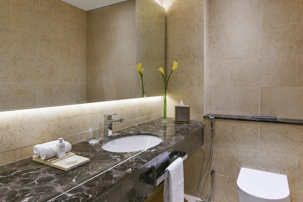 A bathroom with a marble sink, a towel rack, a glass of water, and a vase with flowers.