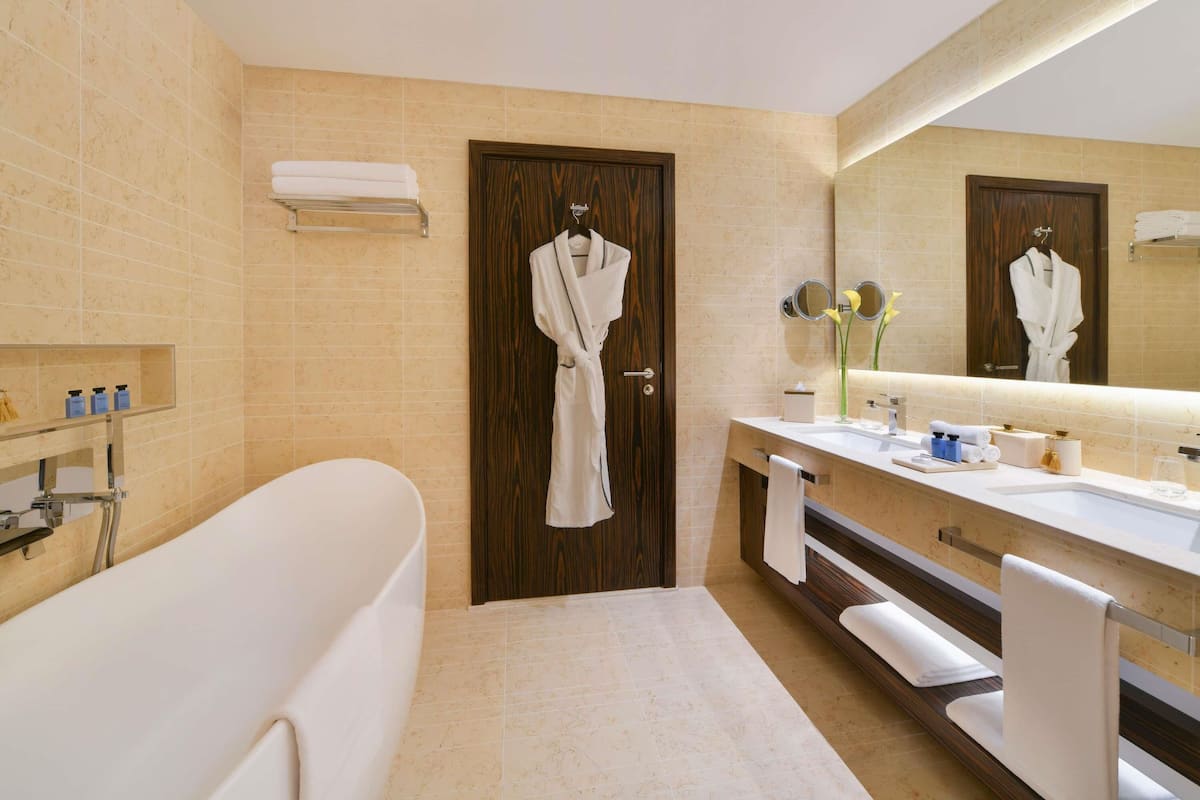 Un baño con bañera, un lavamanos con artículos de aseo, un espejo y una bata colgada en la puerta.