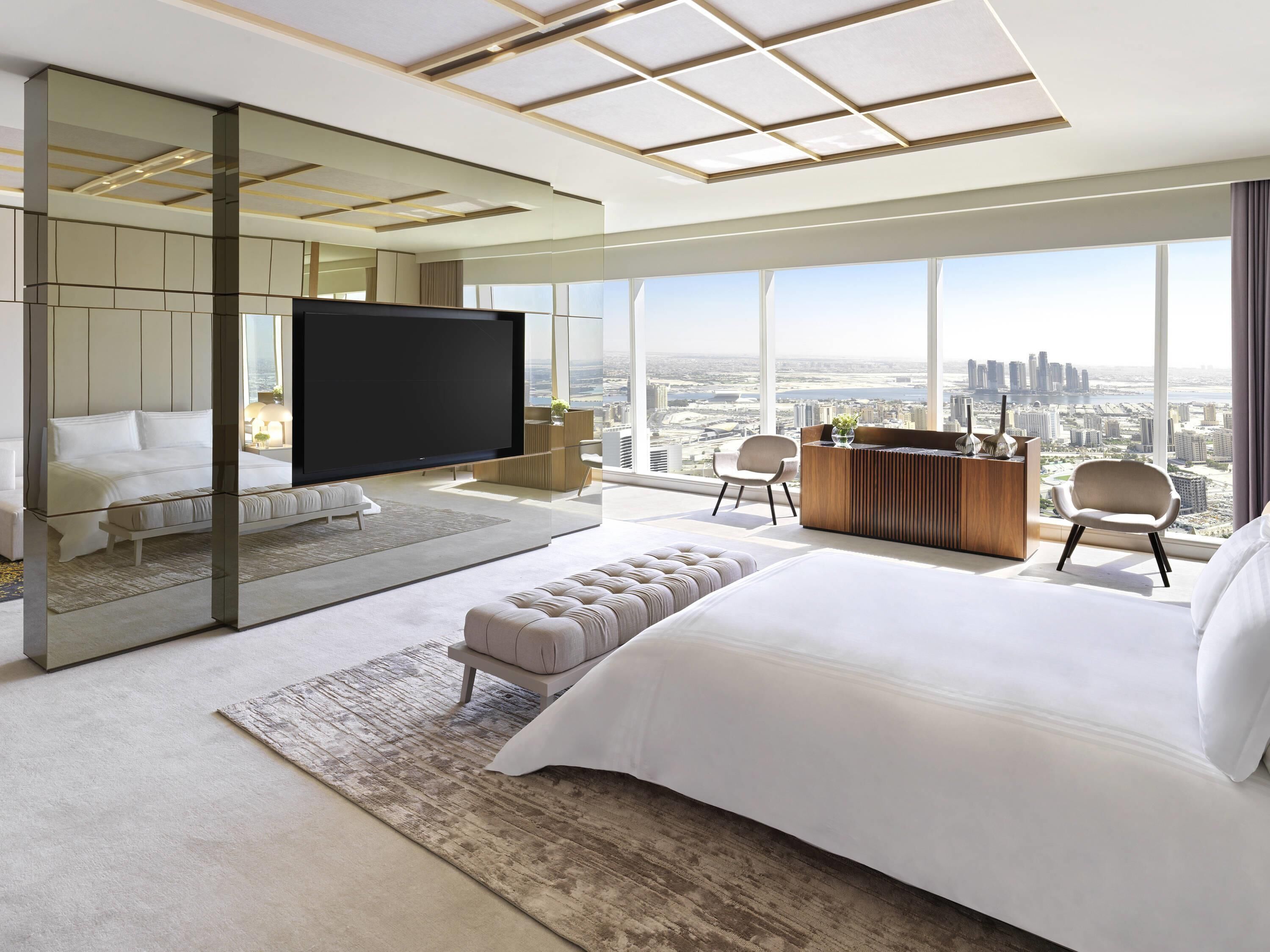 A modern hotel room with a large bed, a TV, a desk, and a view of the city.