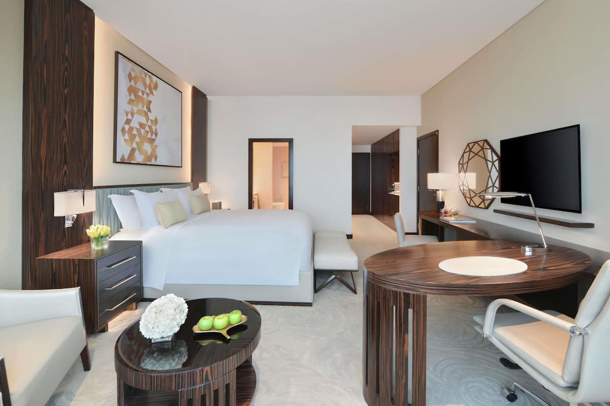 A modern hotel room with a large bed, a desk, a chair, a TV, and a decorative wall piece.