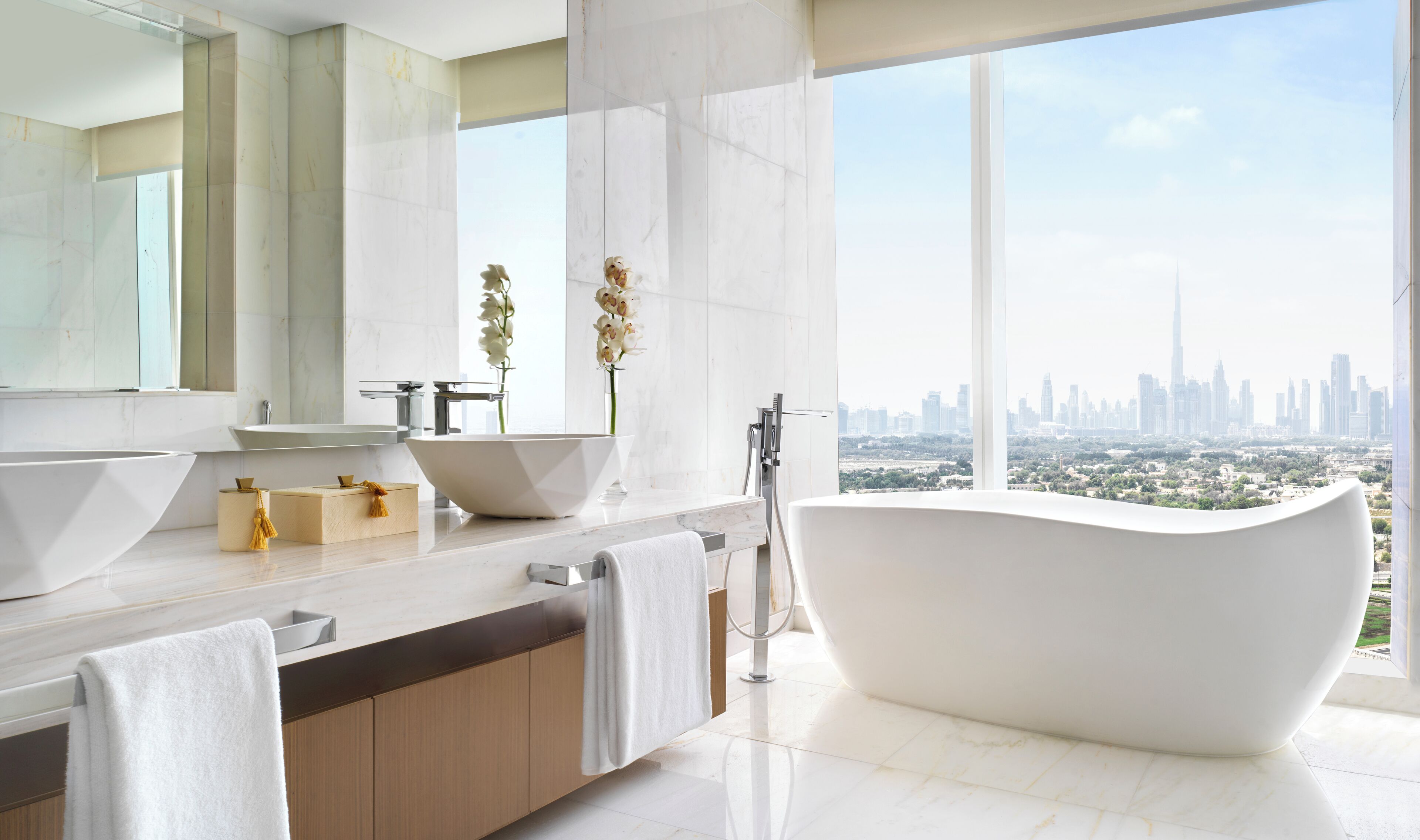Een moderne badkamer met een vrijstaand bad, een grote spiegel en uitzicht op een stadshemelbeeld.