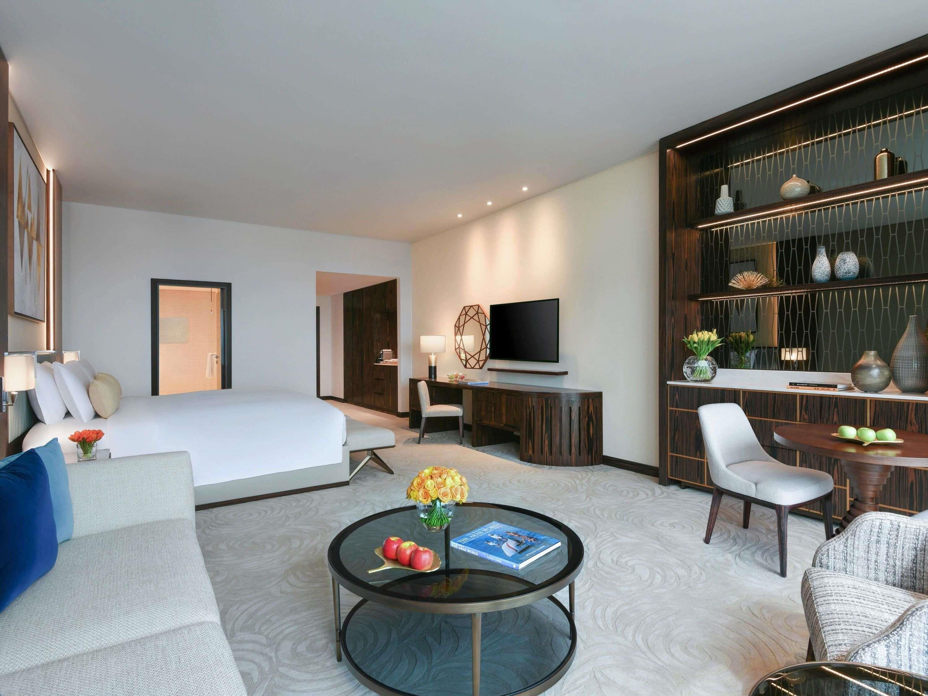 A hotel room with a bed, a TV, a desk, a chair, a coffee table, and a bookshelf.
