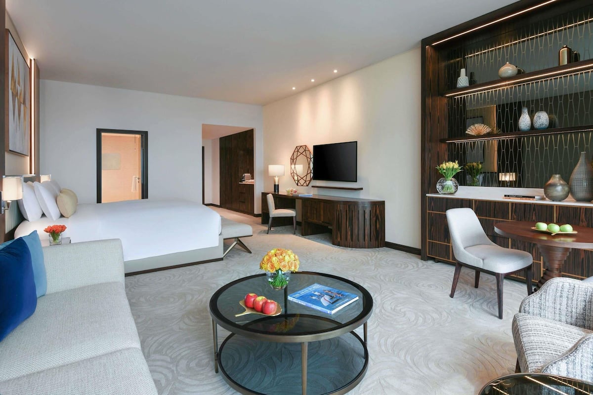 A hotel room with a bed, a TV, a desk, a chair, a coffee table, and a bookshelf.