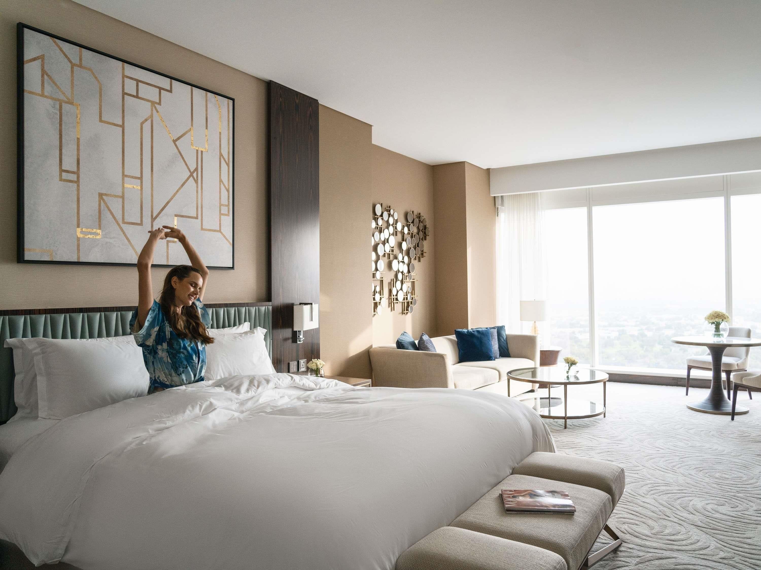 A hotel room with a large bed, a sofa, a coffee table, and a view of the city.