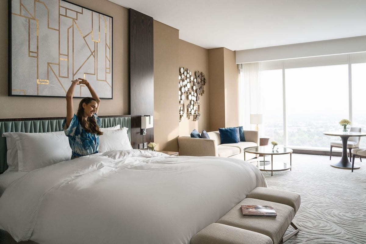 A hotel room with a large bed, a sofa, a coffee table, and a view of the city.