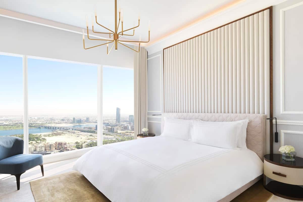 A modern hotel room with a large bed, a view of the city, and a stylish chandelier.