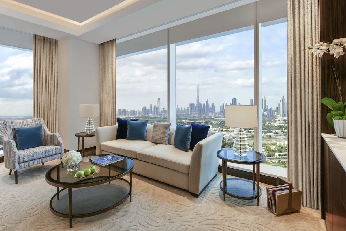 A modern living room with a sofa, armchairs, and a coffee table. Large windows offer a city skyline view.