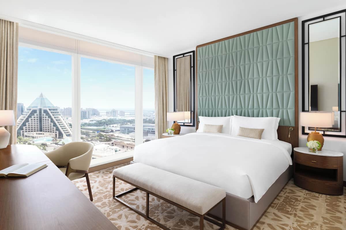 A hotel room with a large bed, a desk, a chair, and a view of a cityscape.