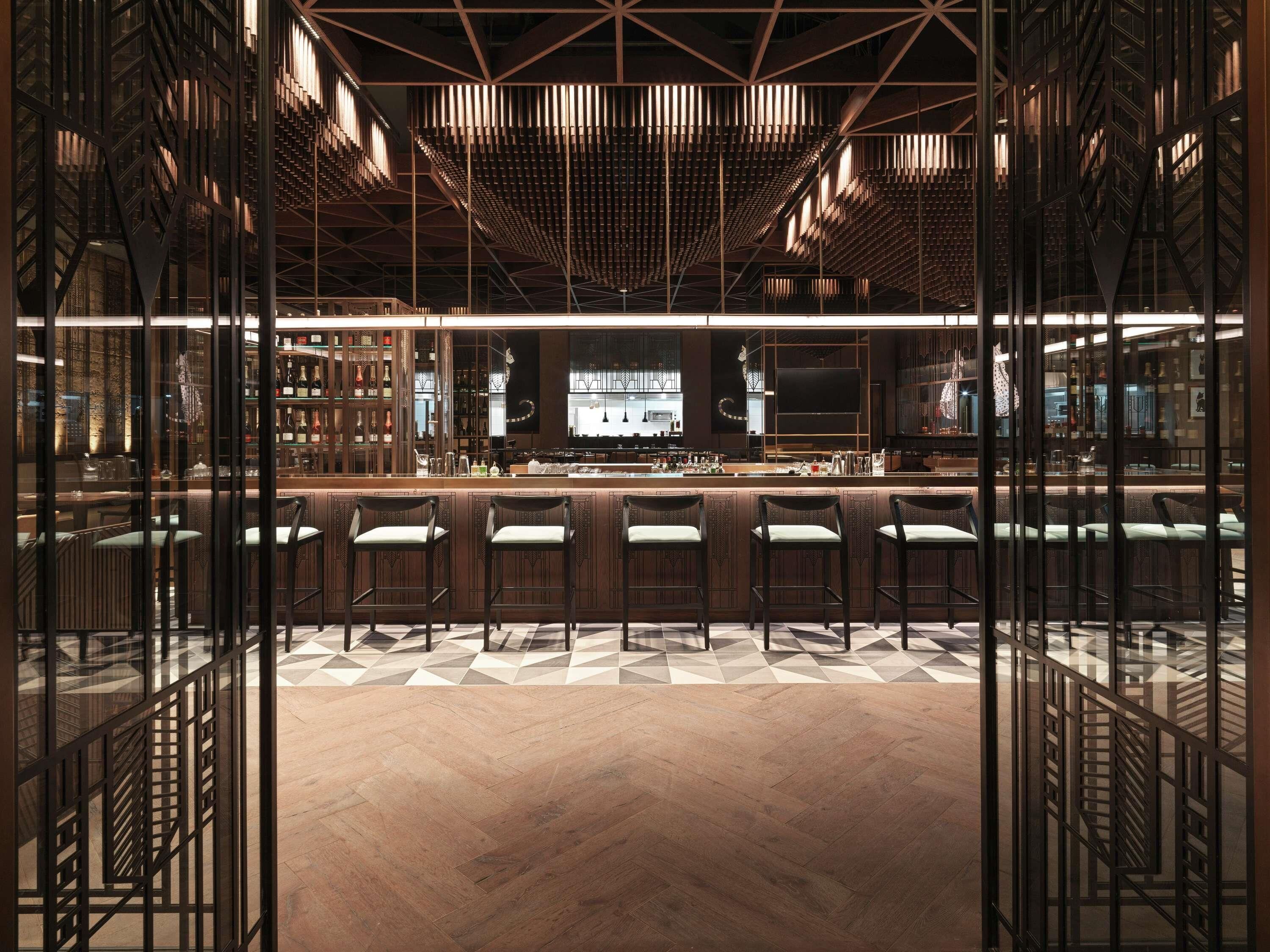 Eine moderne Bar mit geometrischem Bodenmuster, einer Bar und Sitzgelegenheiten mit Blick durch eine strukturierte Glasscheibe.