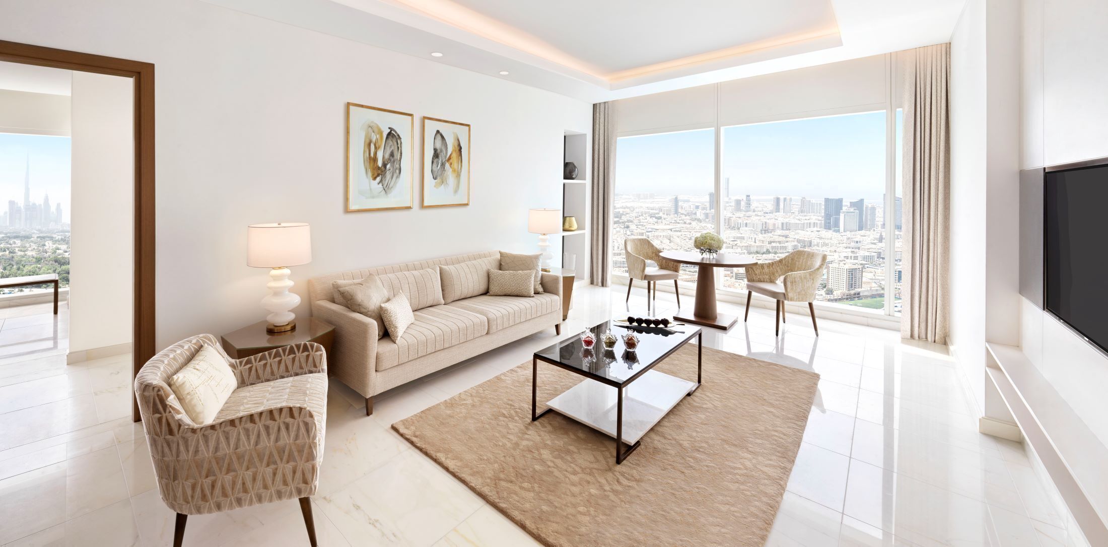 Un salon moderne avec un canapé, une table basse et des fauteuils, une vue sur la ville et des œuvres d’art accrochées au mur.