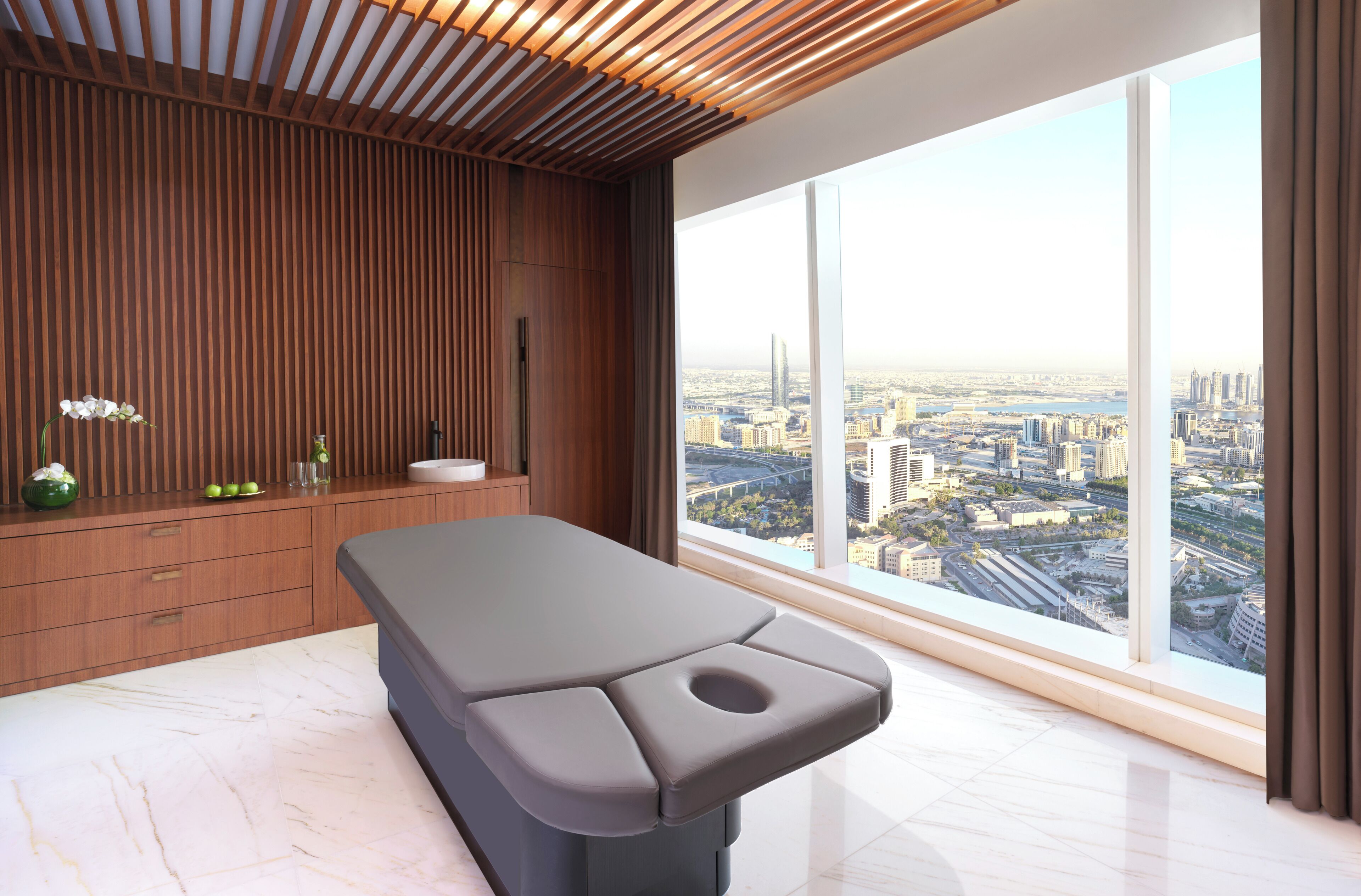A modern room with a large window, a wooden wall panel, and a massage table.